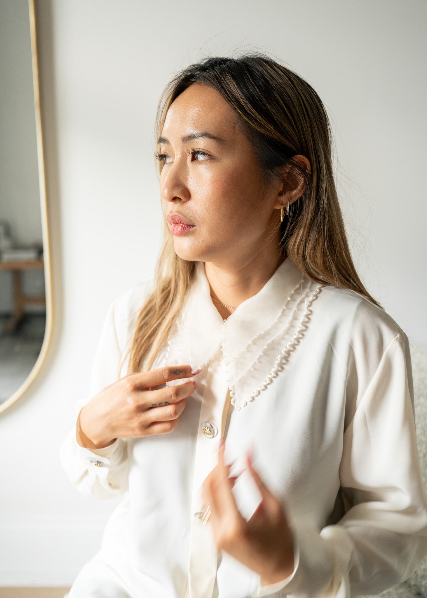 Woman wearing a white blouse with beaded details, standing against a plain wall.