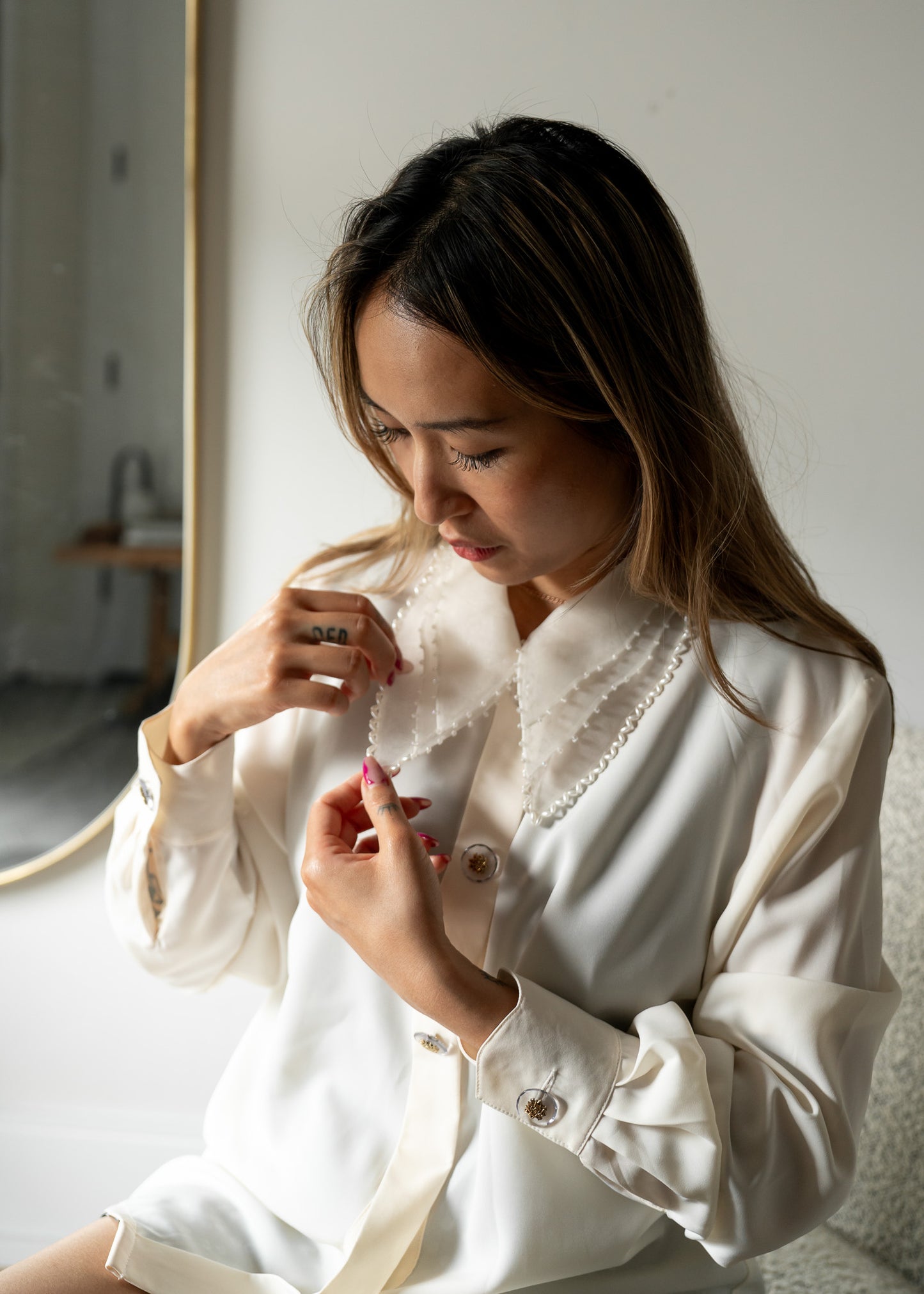 Woman wearing a white blouse with beaded details in a softly lit room.