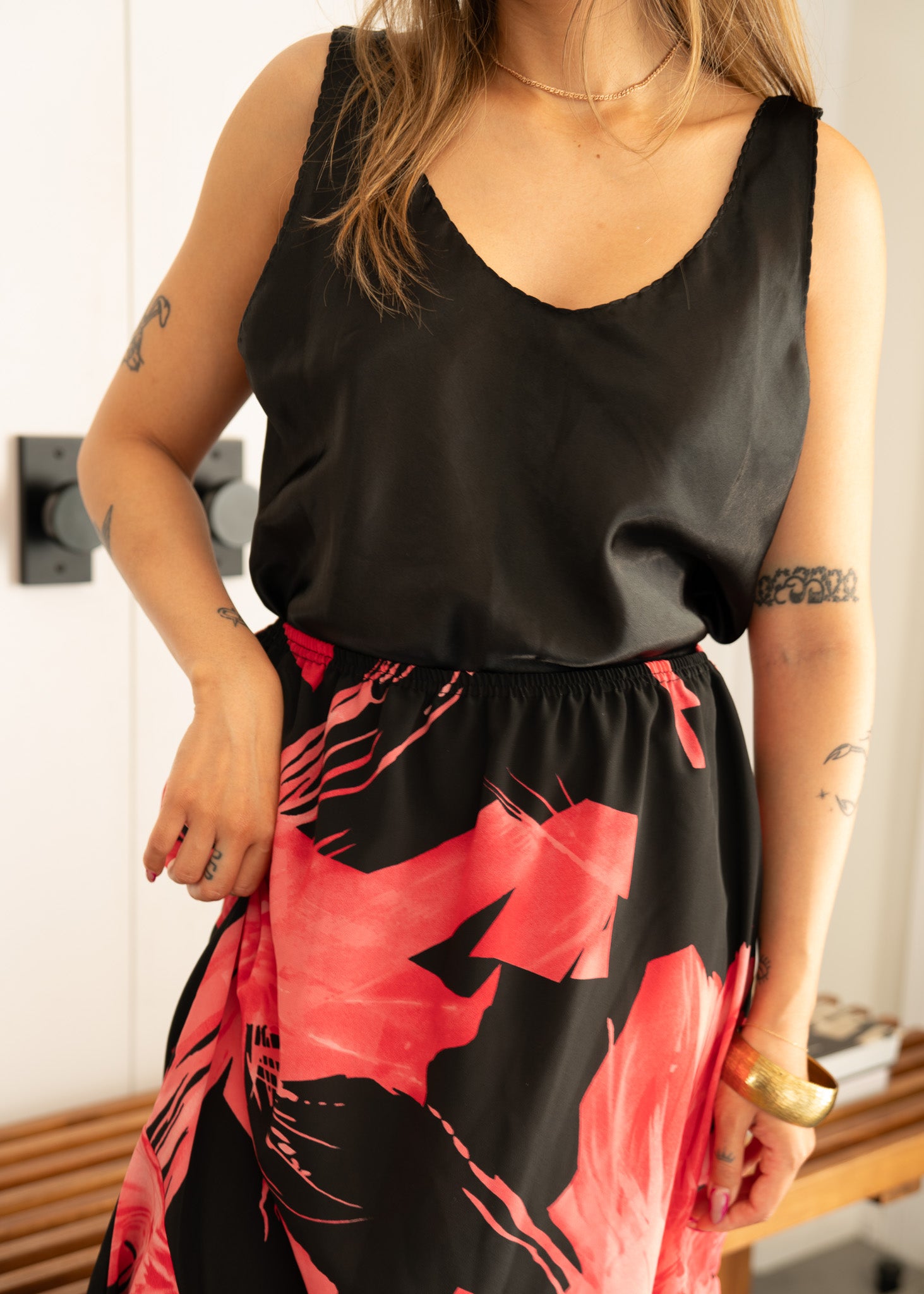 Person wearing a vintage black sleeveless top and pink and black floral skirt indoors.