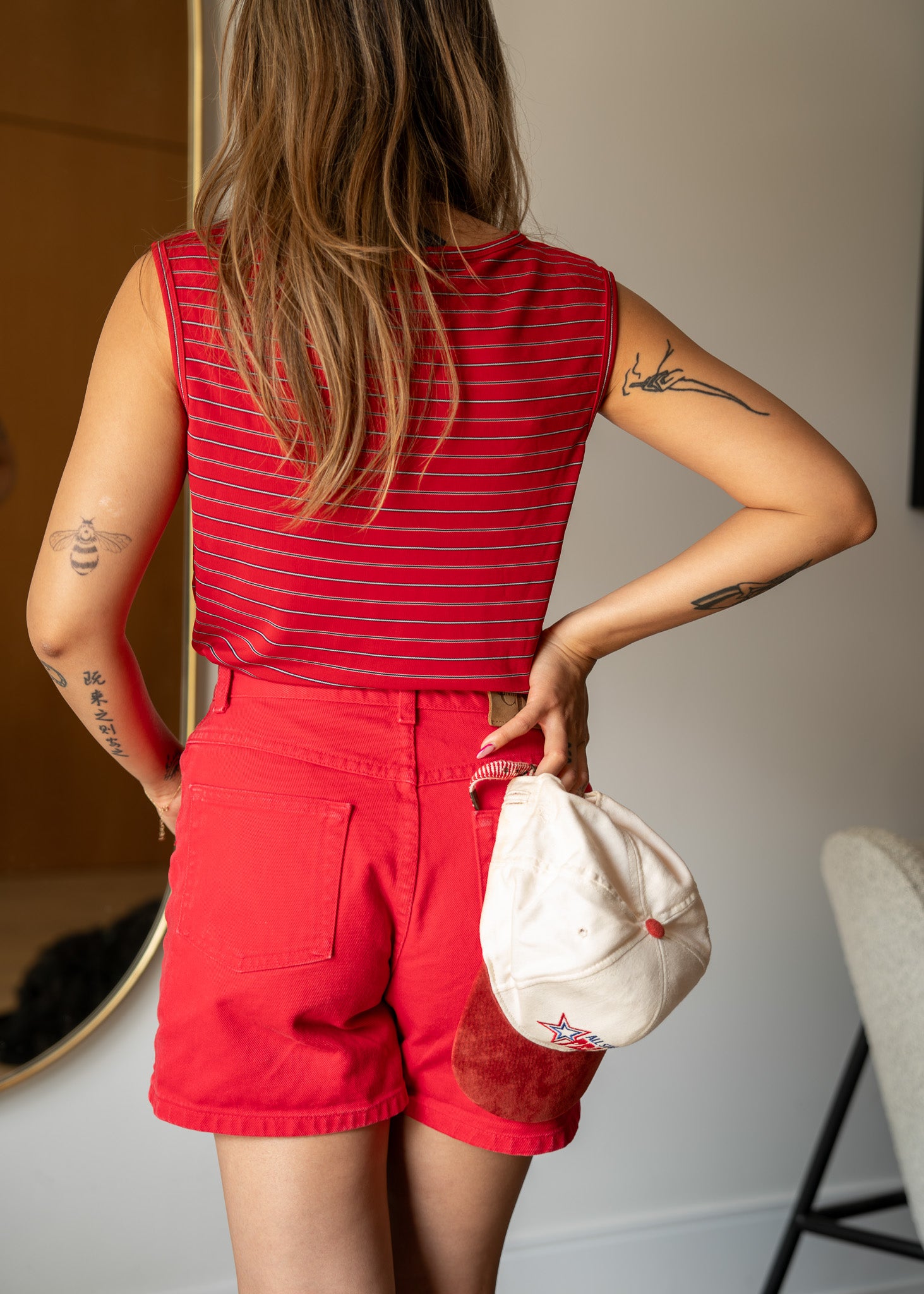 Person wearing a red sleeveless top and high waisted red denim shorts, holding a white cap with a red logo.