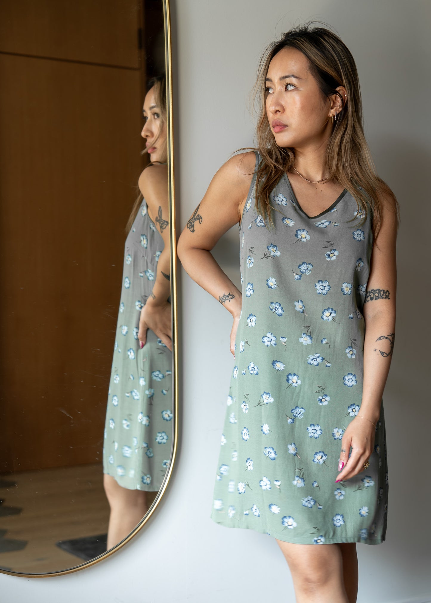 Woman wearing a green floral dress standing in front of a mirror.