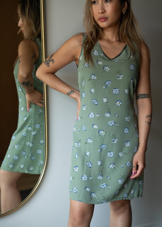 Woman wearing a green floral dress standing in front of a mirror.