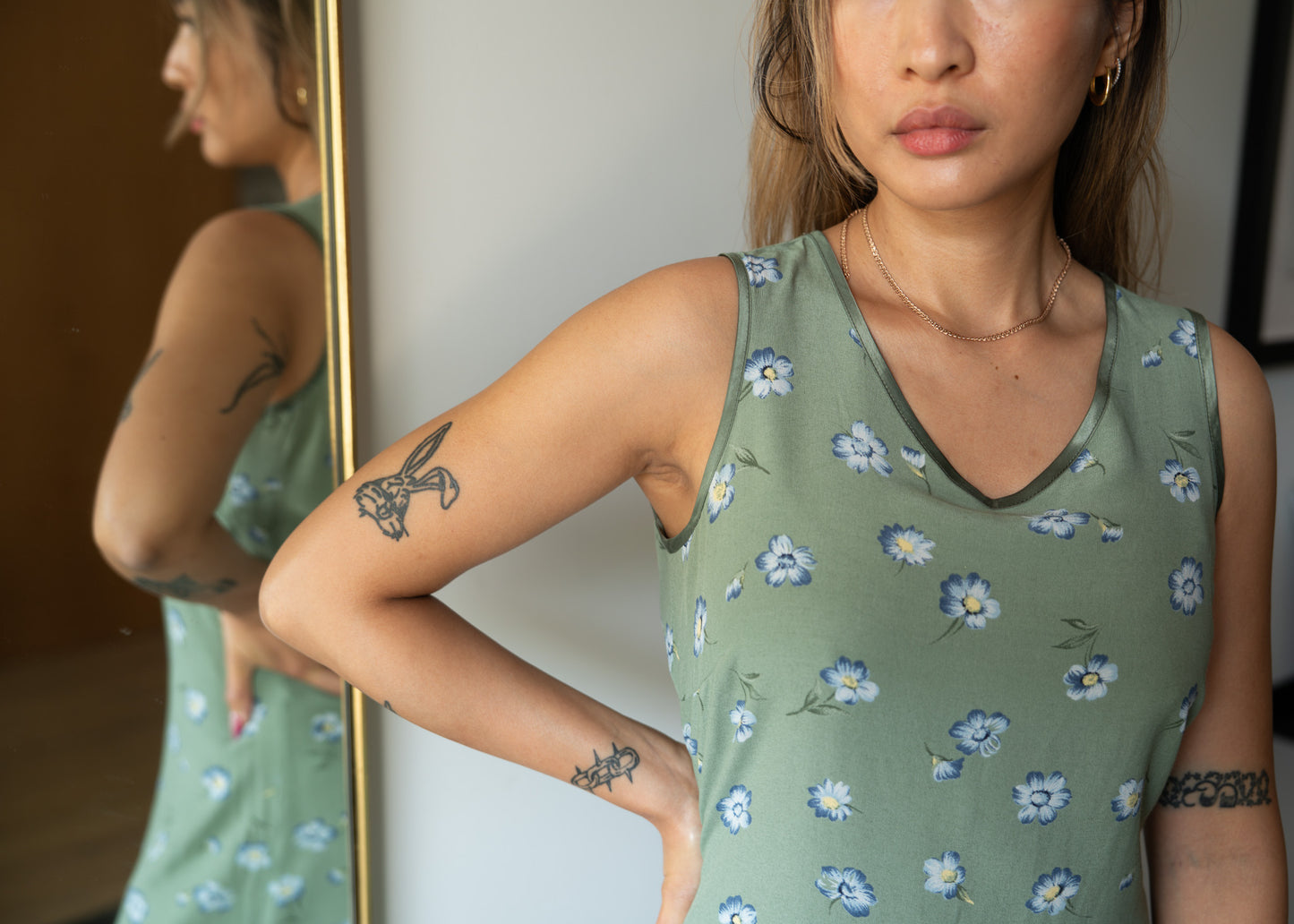 Woman wearing a green floral sleeveless dress in front of a mirror.