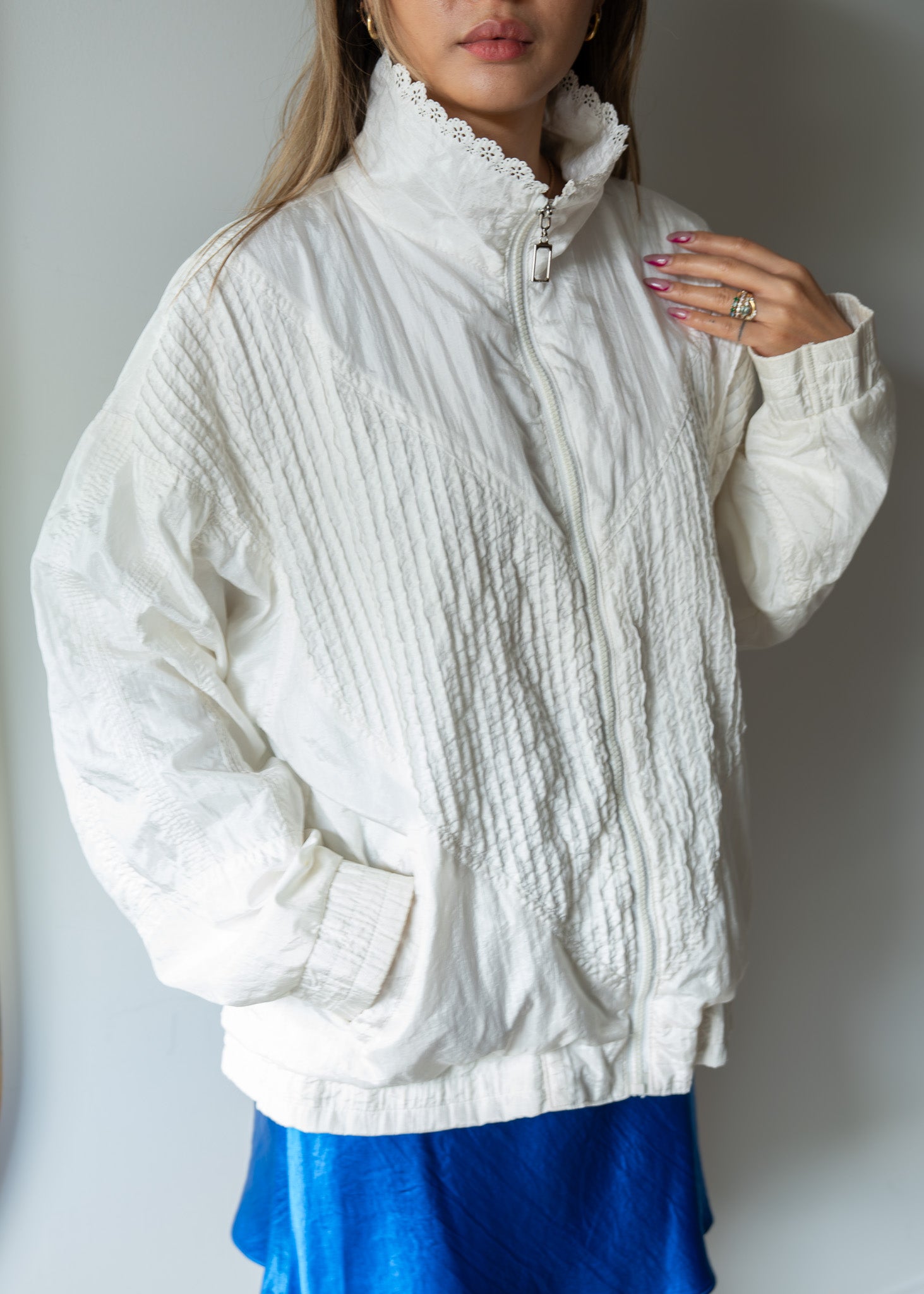 Person wearing a white textured windbreaker over a blue skirt against a plain background