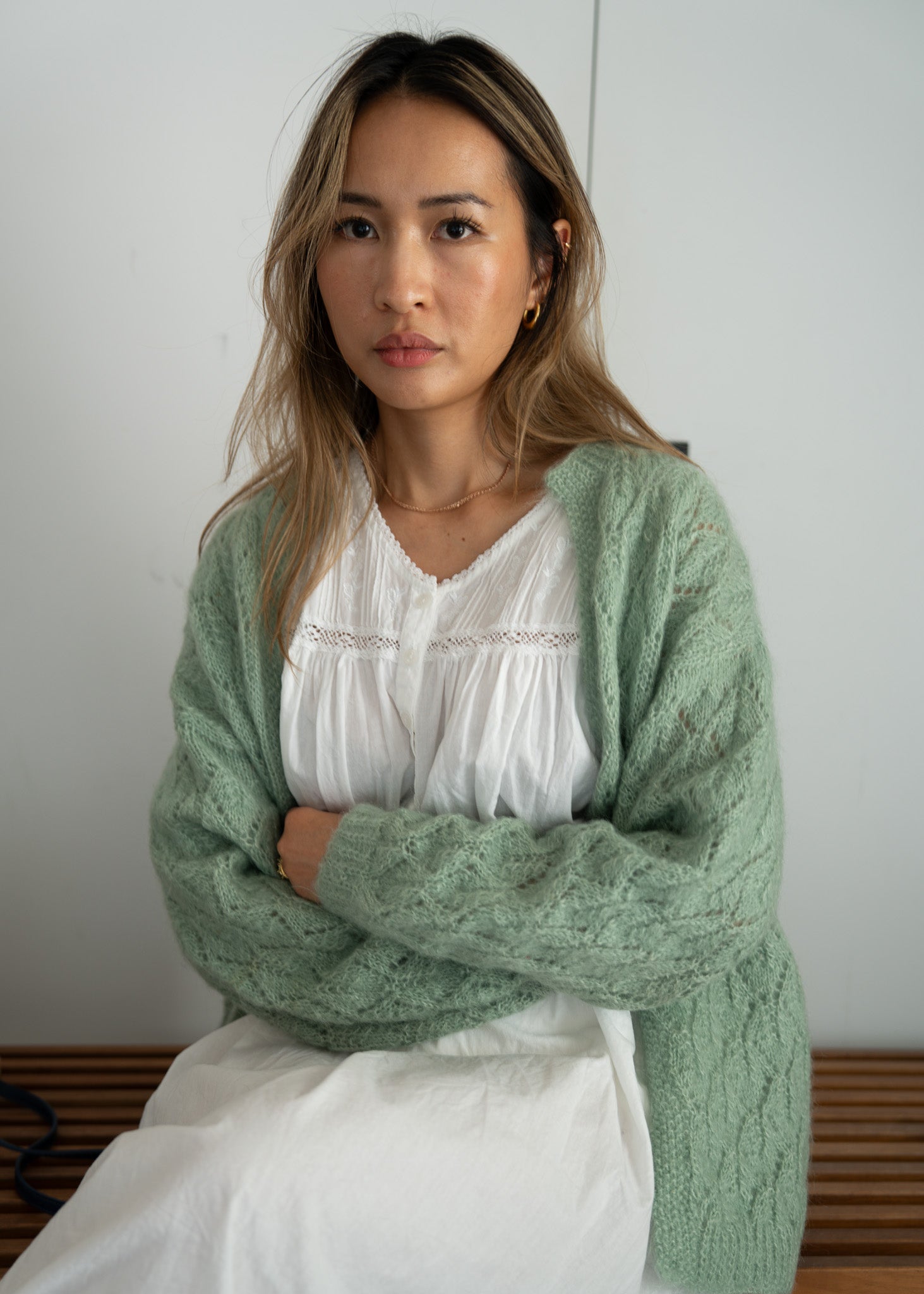 Woman wearing a green knitted cardigan over a white cotton dress against a plain background
