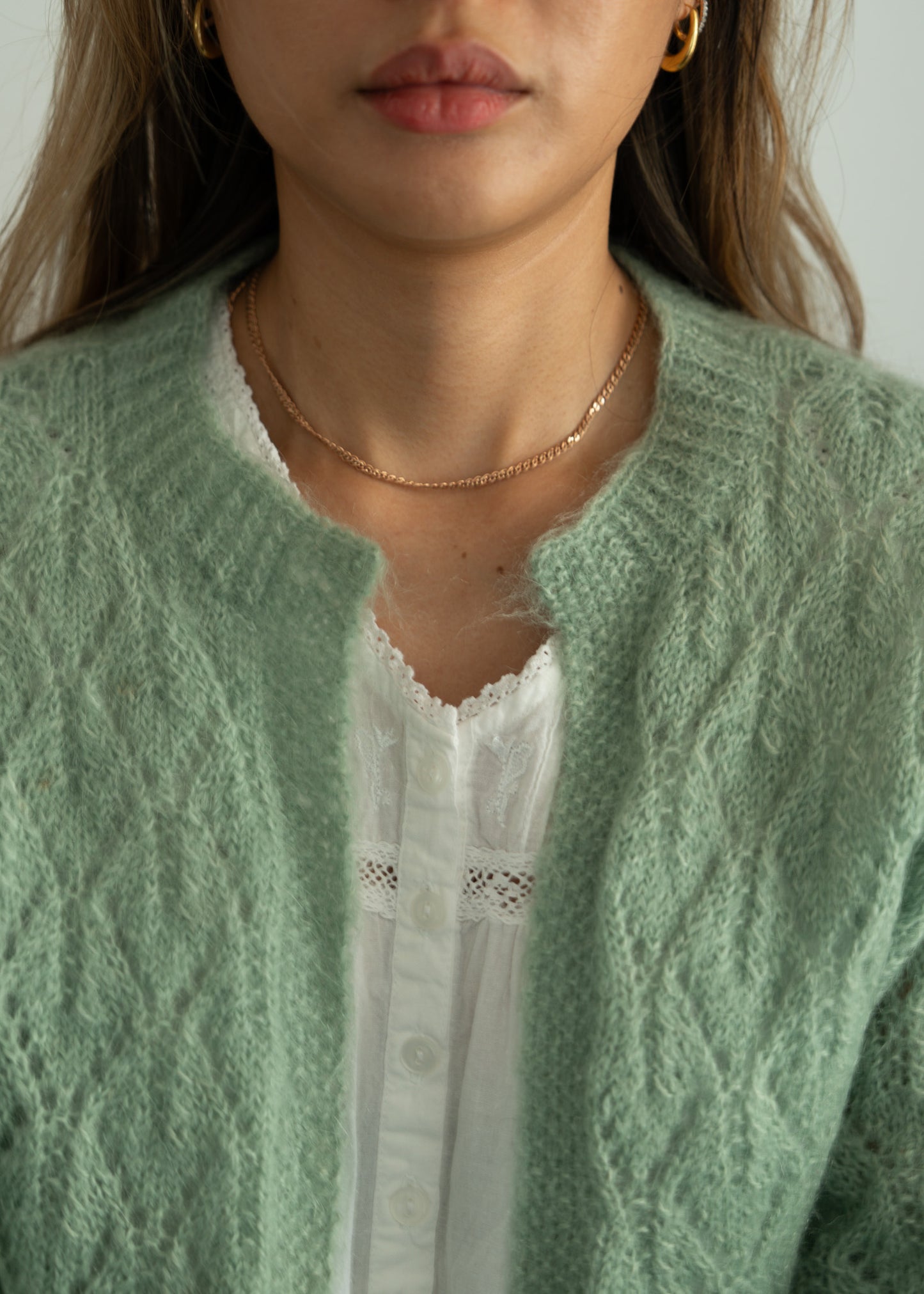 Person wearing a green knitted cardigan over a white cotton dress with a neutral background