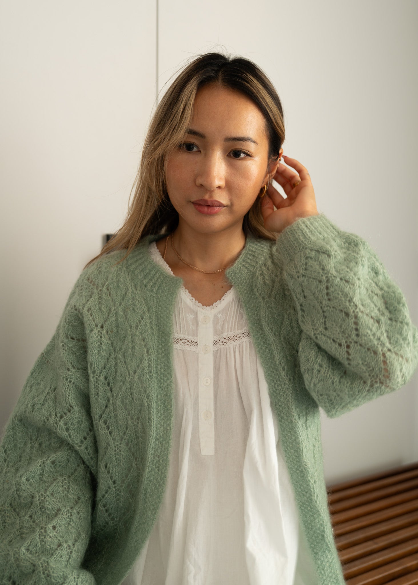 Woman wearing a light green knitted cardigan over a white cotton dress against a plain background