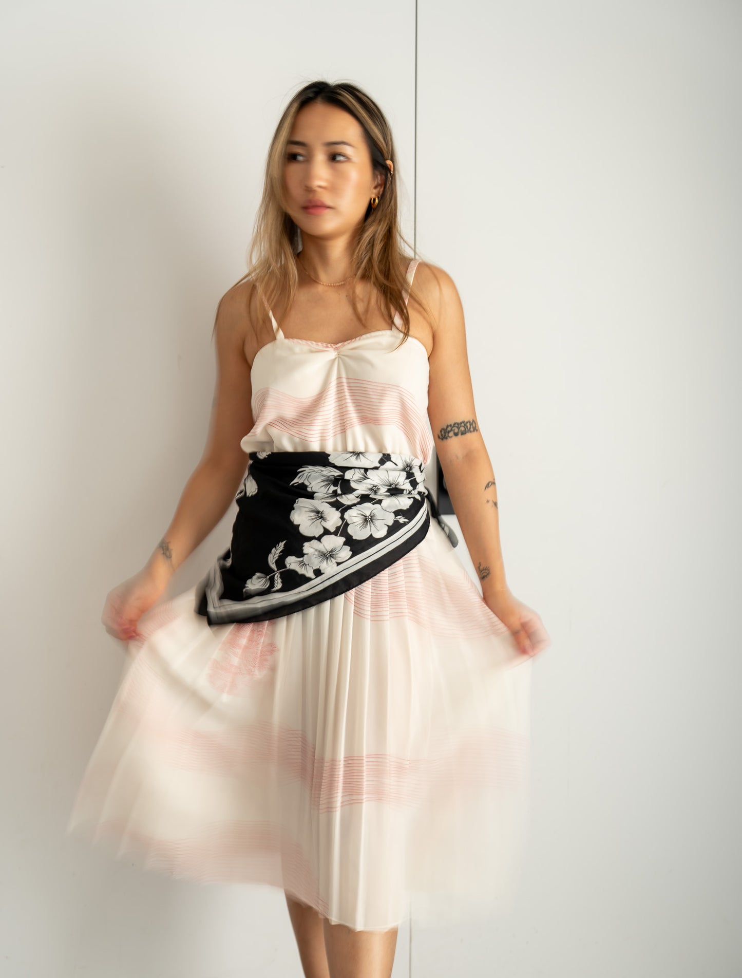 Woman wearing a white and pink dress with a black floral scarf around her waist against a white background