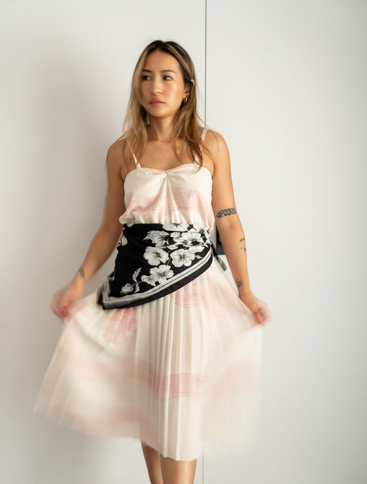 Woman wearing a white and pink dress with a black floral scarf around her waist against a white background