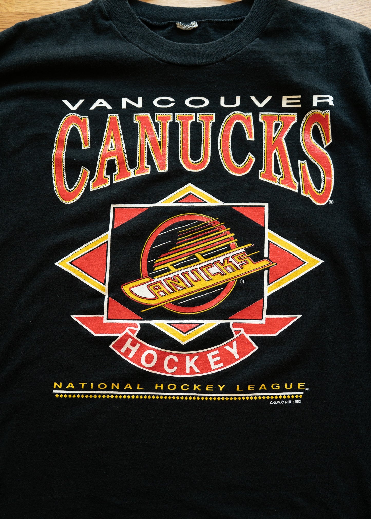 Black t-shirt with Vancouver Canucks logo and text on a wooden surface