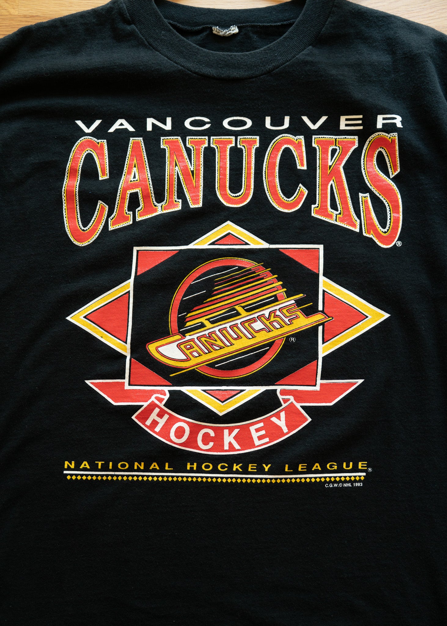 Black t-shirt with Vancouver Canucks logo and text on a wooden surface