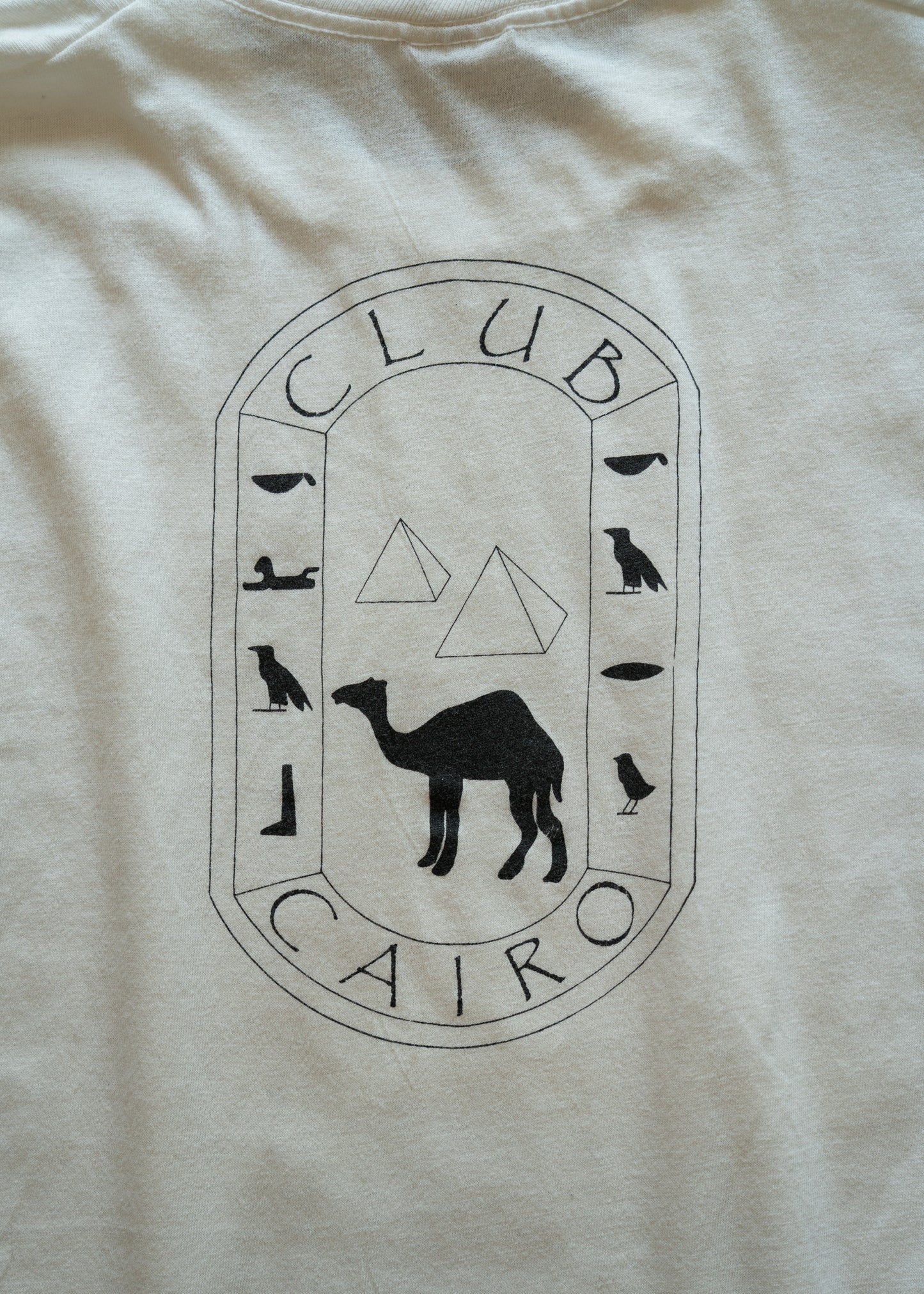 Beige t-shirt with 'Club Cairo' logo featuring a camel and Egyptian hieroglyphs.