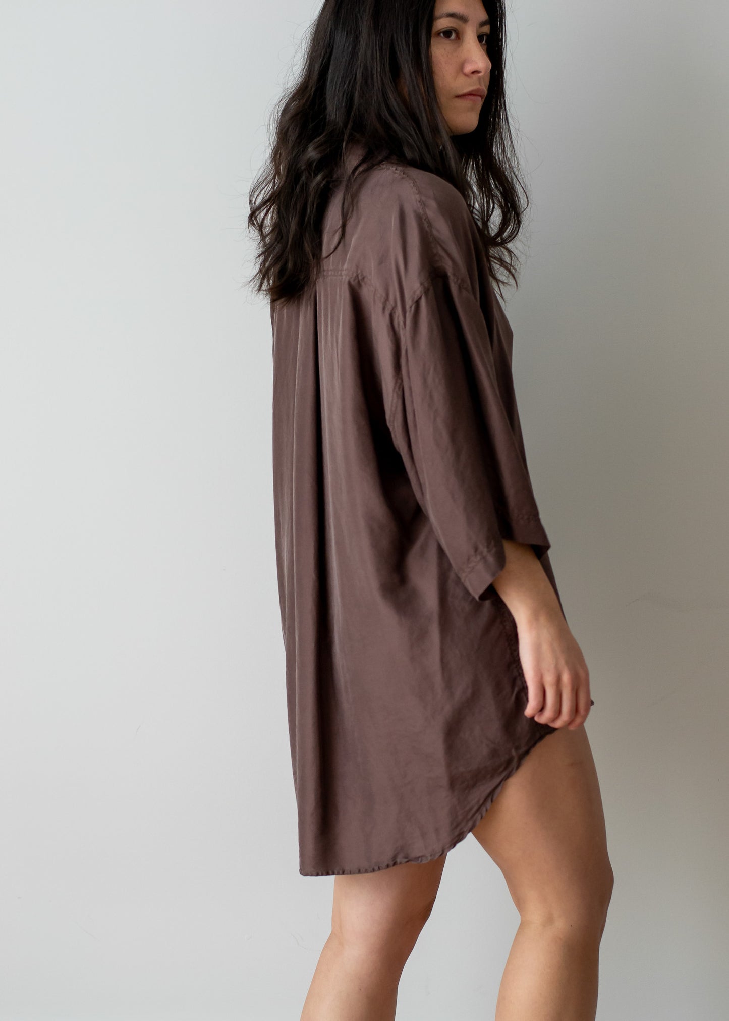 Woman wearing a brown oversized silk shirt against a plain background