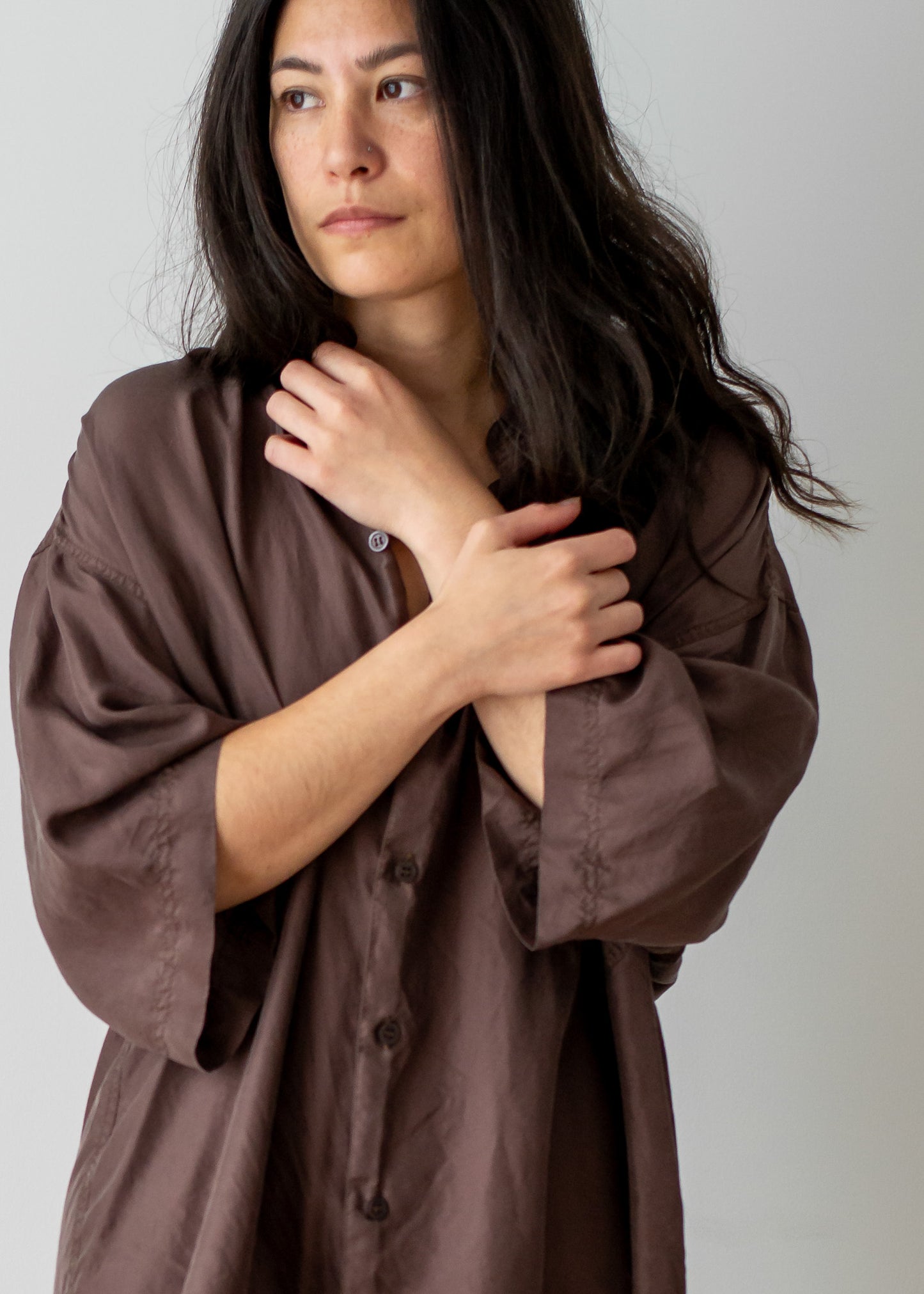Woman wearing a brown silk shirt against a plain background