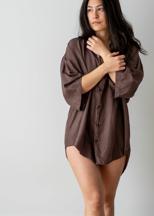 Woman wearing a brown silk oversized short sleeve shirt against a plain background