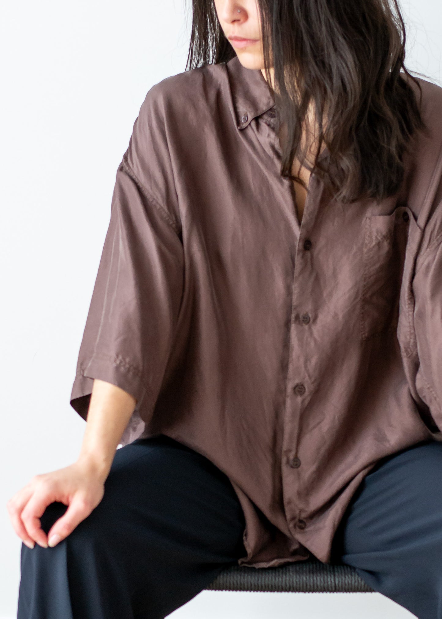 Person wearing a brown silk button-up shirt sitting on a black chair.