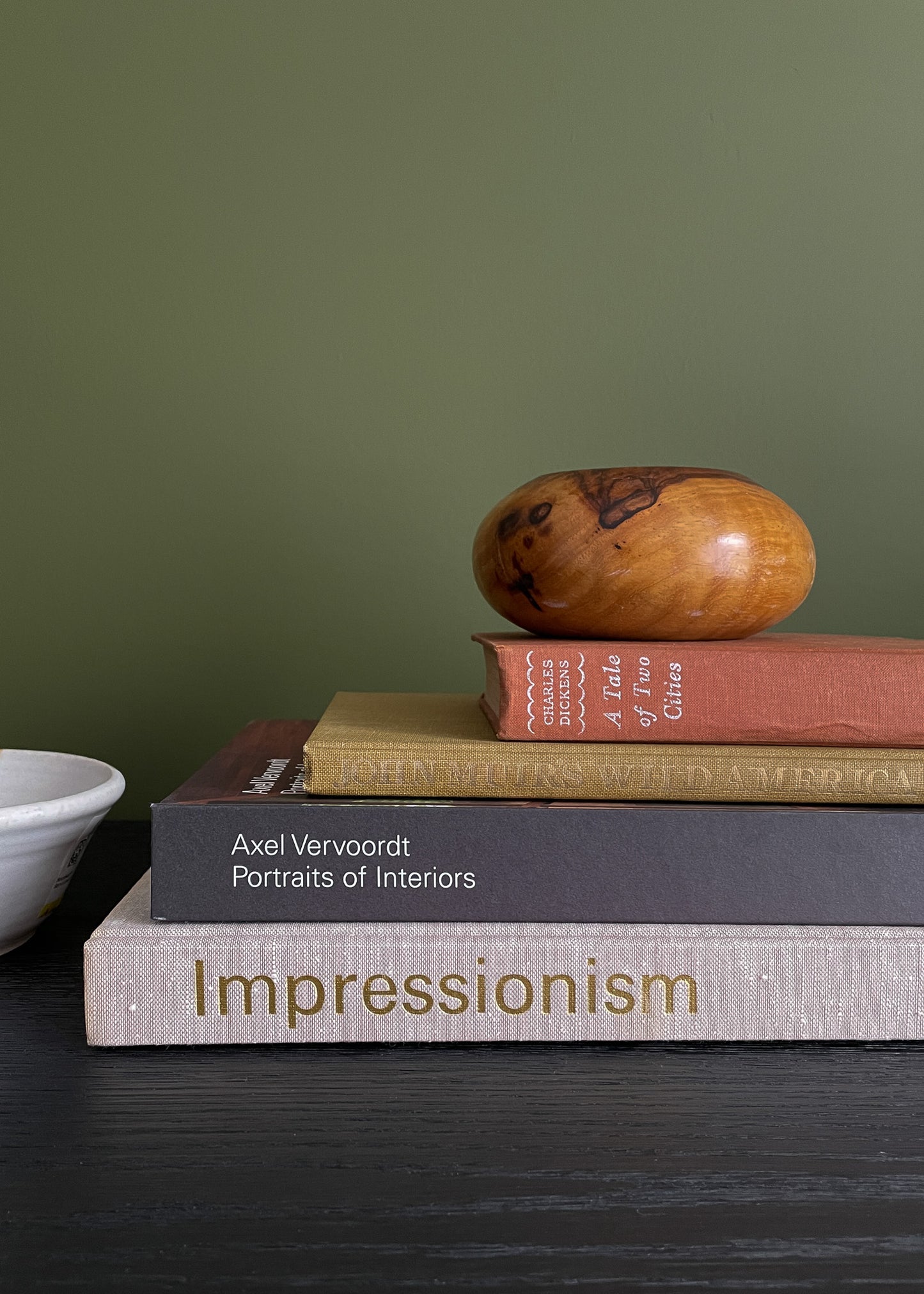 Stack of books with a vintage wooden bowl on top against a green wall