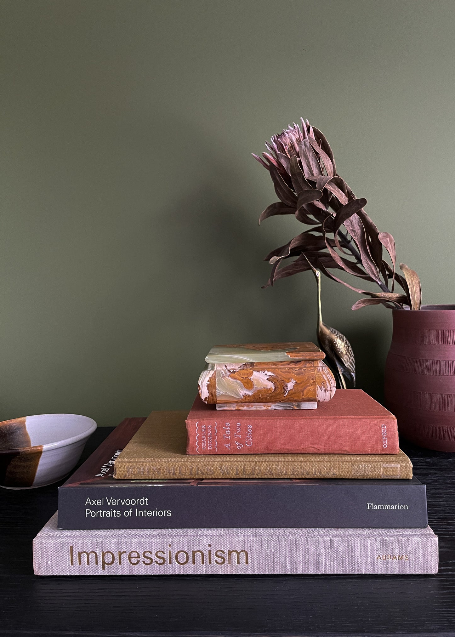 Stack of books with a vintage onyx box and a plant on a dark surface against a green wall
