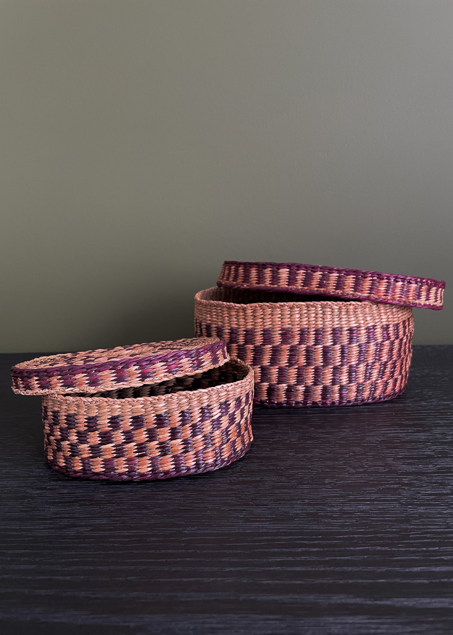 Two vintage woven baskets with a purple and neutral pattern on a dark surface and green background