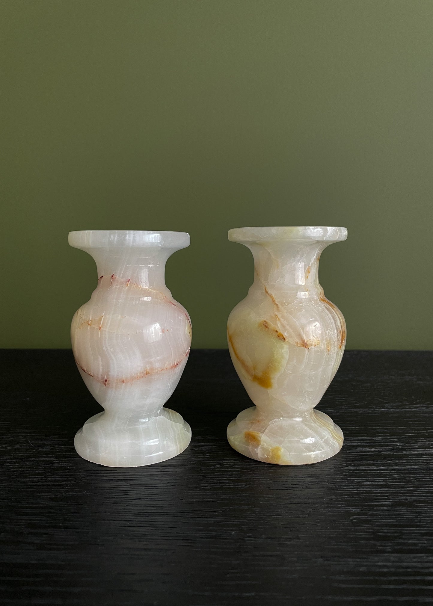 Two vintage onyx candle holders with marbled patterns on a dark surface and green background
